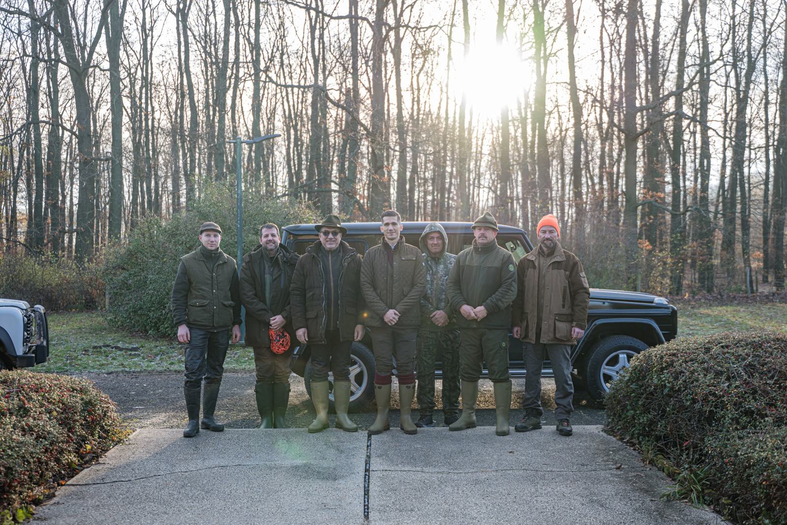 The hunting party standing together in front of an off-road vehicle at the edge of the forest